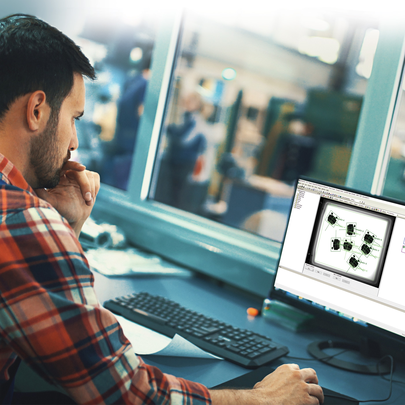 A man in a manufacturing environment looking at RC+ software on a computer screen