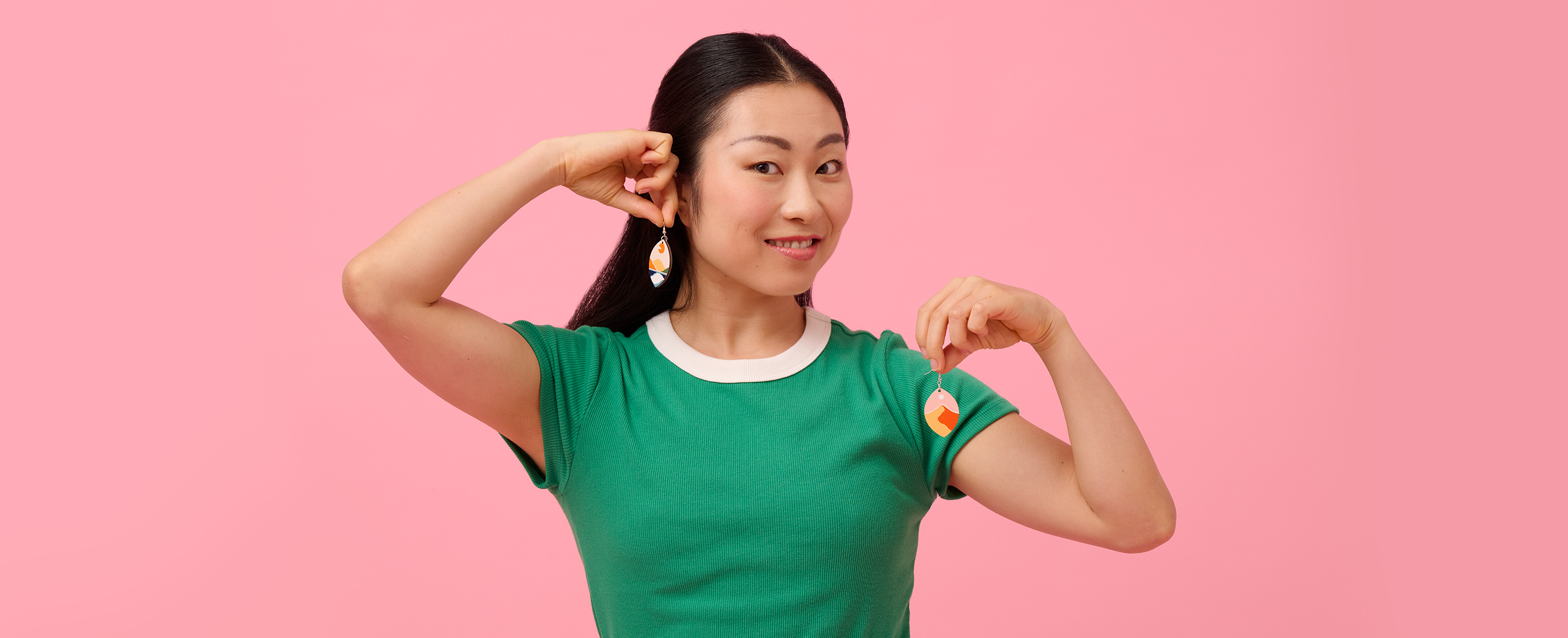 A woman putting on earrings printed with landscape patterns.