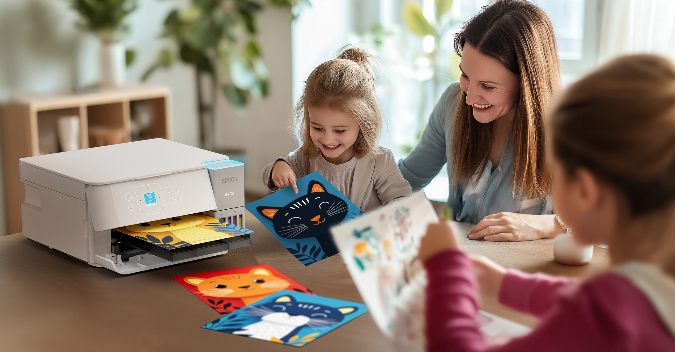 A mother and her two daughters gather around a table with an EcoTank printer, looking at printed cat illustrations.