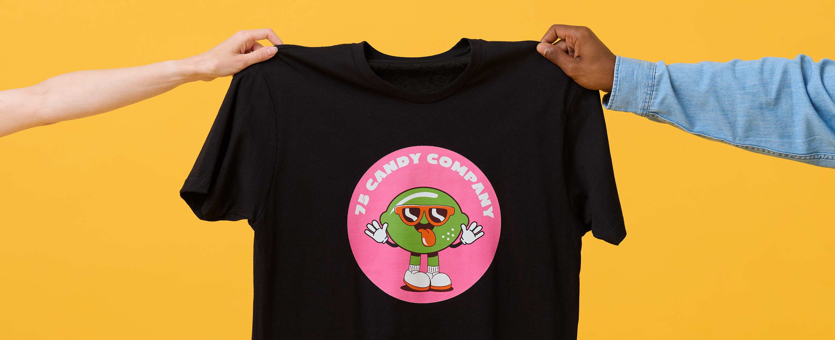 Two hands hold up t-shirt printed with candy company mascot.