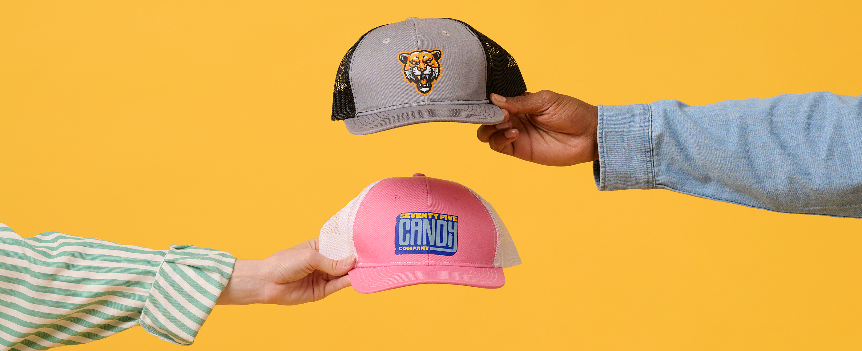 Two outstretched arms holding hats printed with tiger and candy designs.
