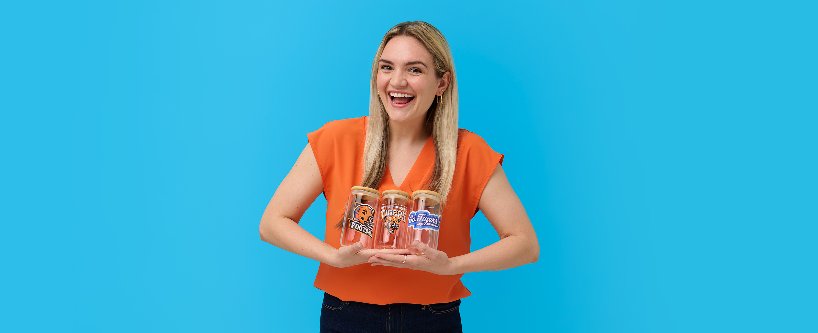 A woman holding glass tumblers printed with high school football team designs.