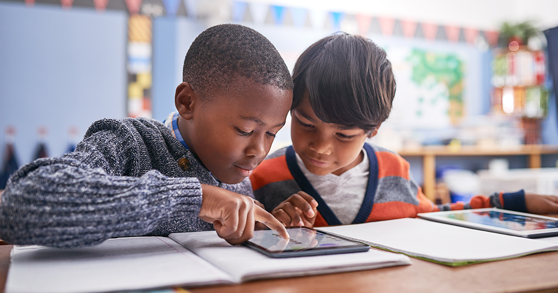Two elementary school boys work on assignment on tablet.