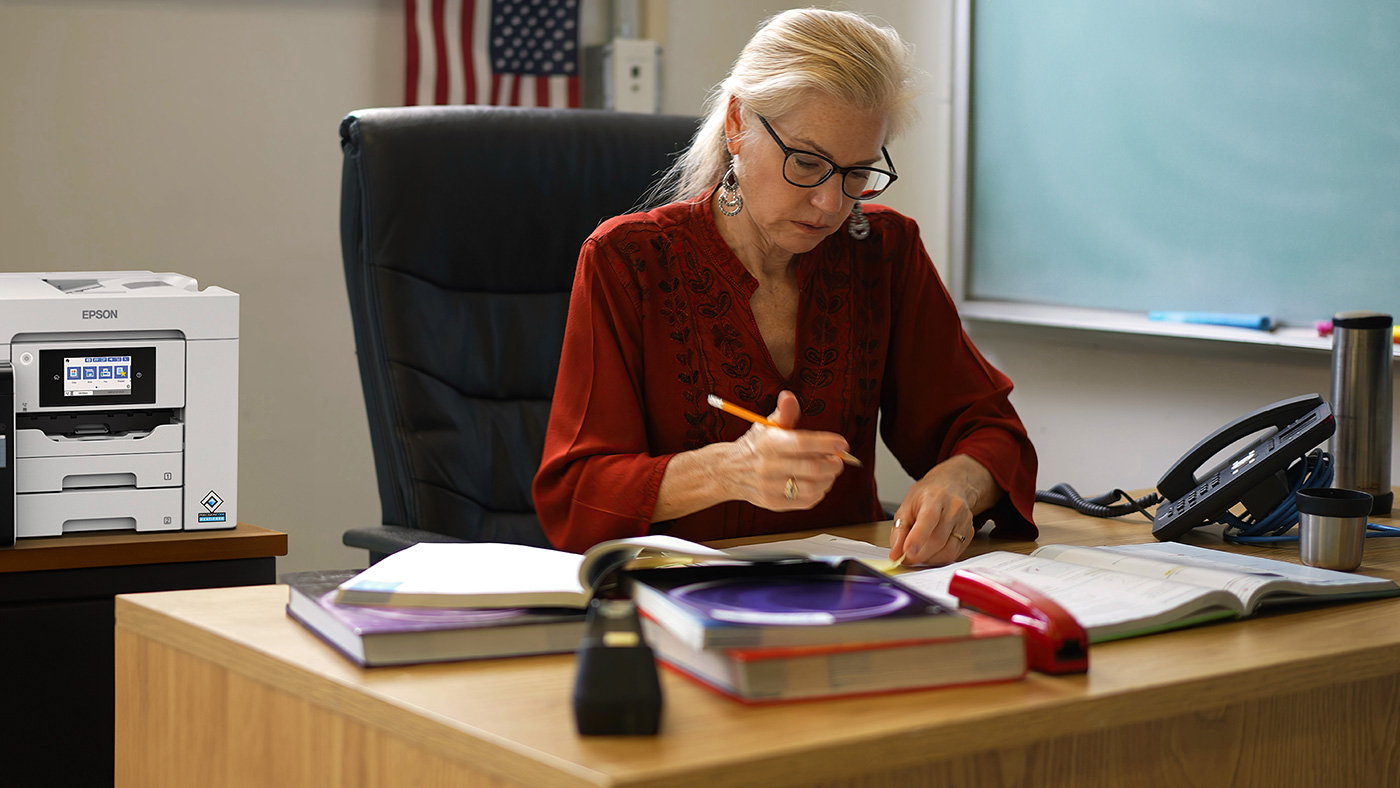 A woman working at a desk, with a business inkjet printer in the background
