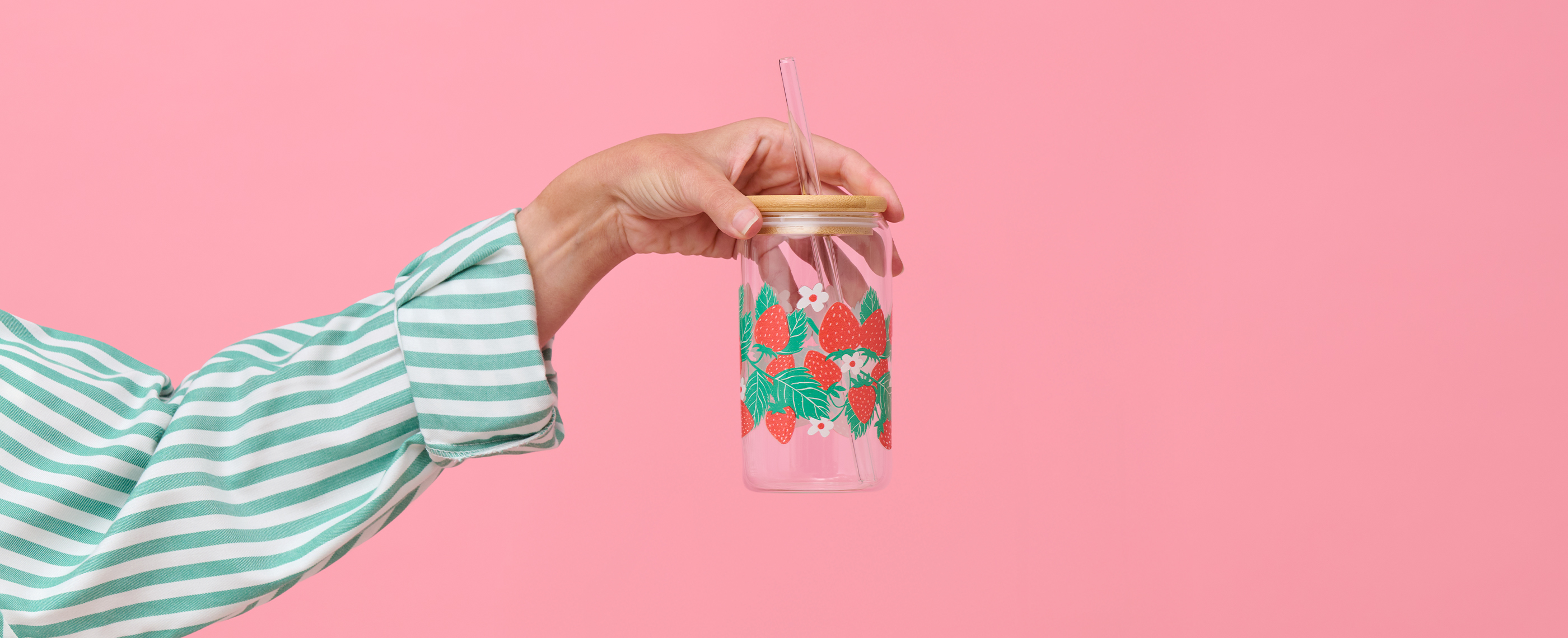 A hand holding a glass tumbler printed with a strawberry pattern.