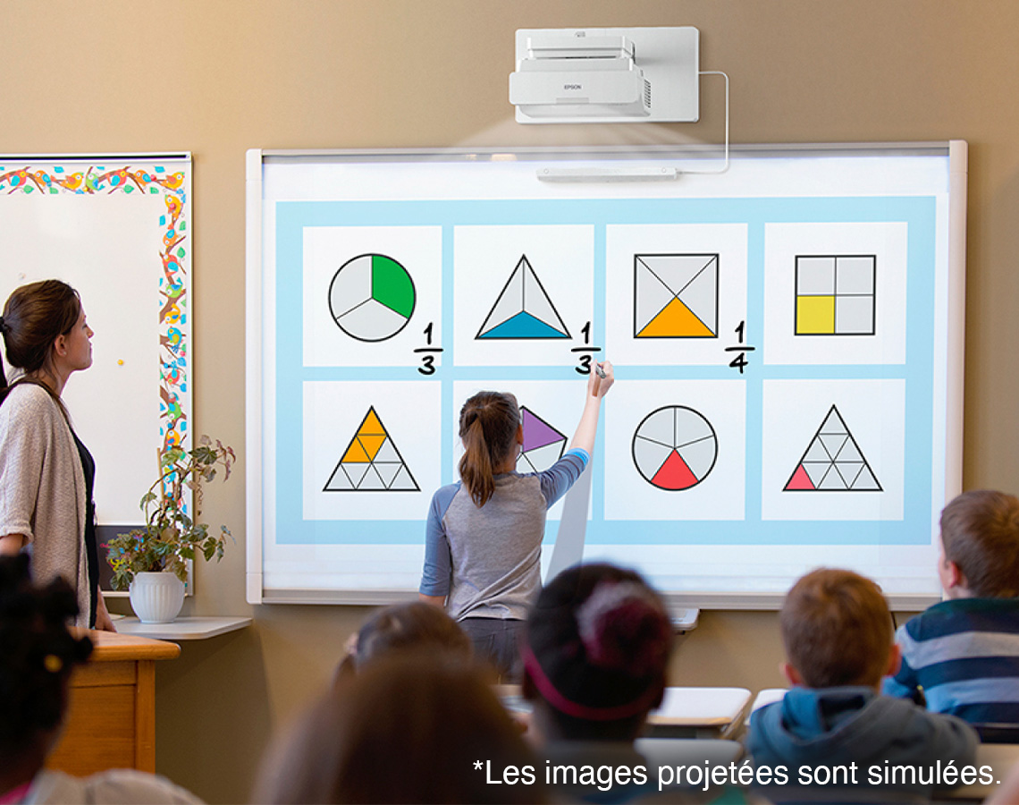A girl writing fractions on a whiteboard with a projected image of various geometric shapes.