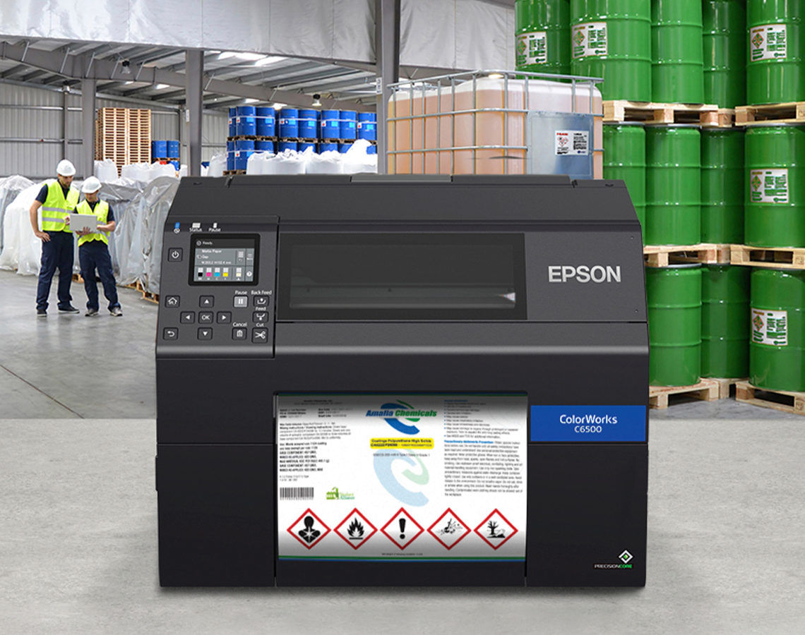 An Epson ColorWorks C6500 printer printng a chemical product label in a warehouse with chemical barrels.