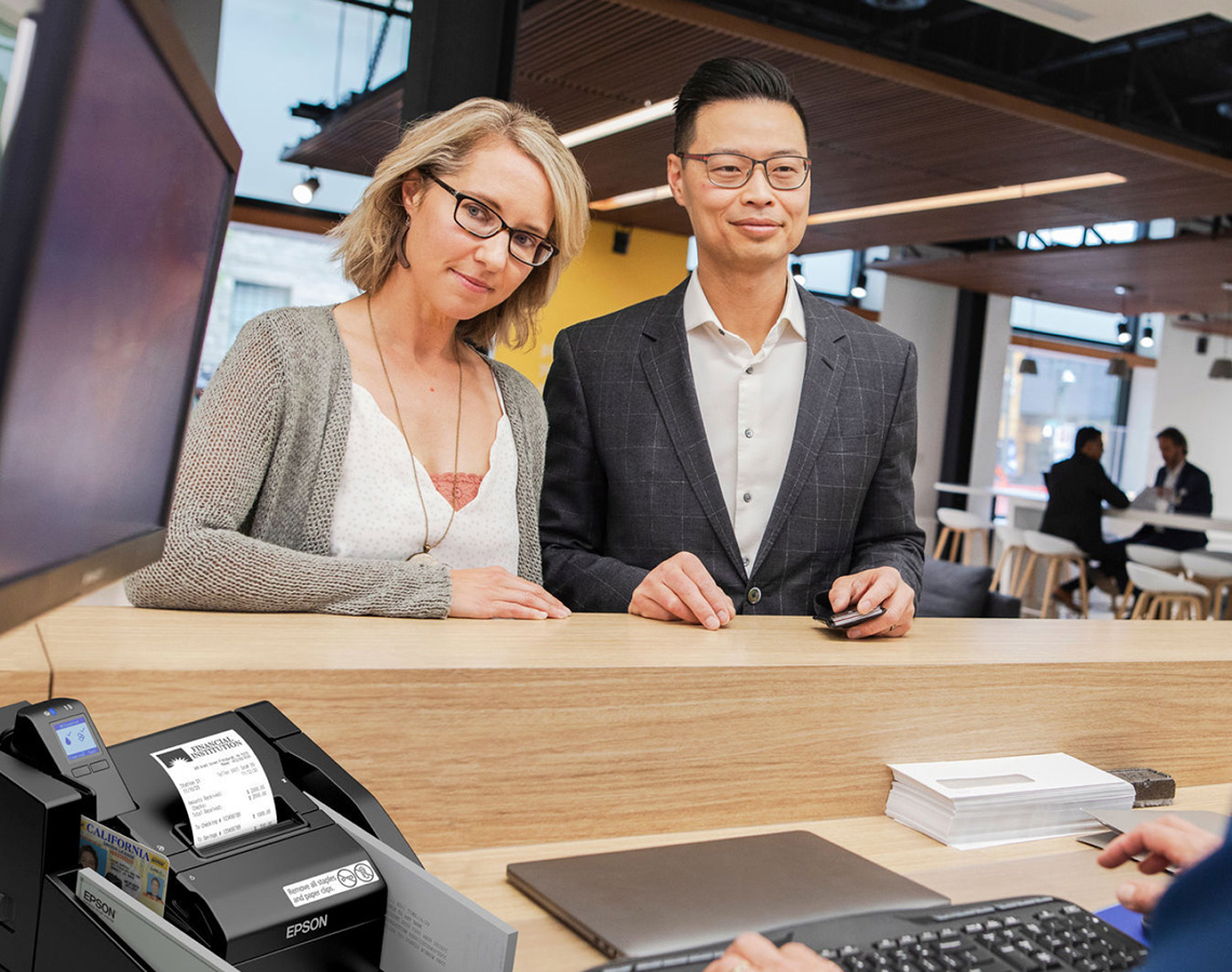 Bank teller printing receipt for two professionals
