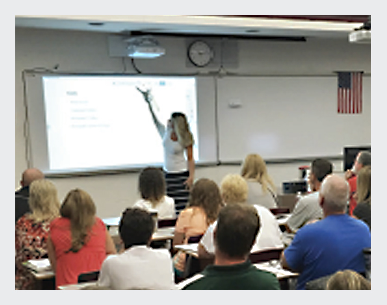 A teacher pointing at a projected screen in front of the class