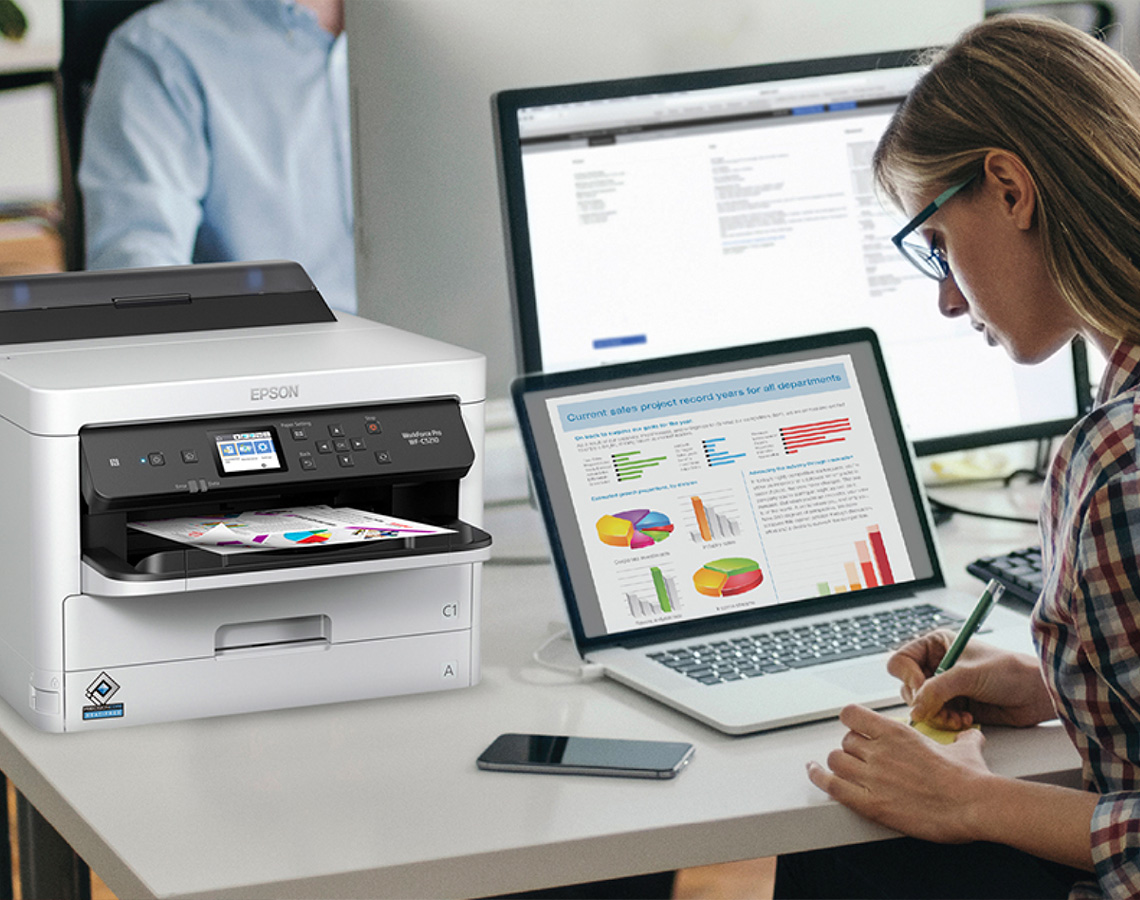 Professional writing at desk with computers and Epson printer
