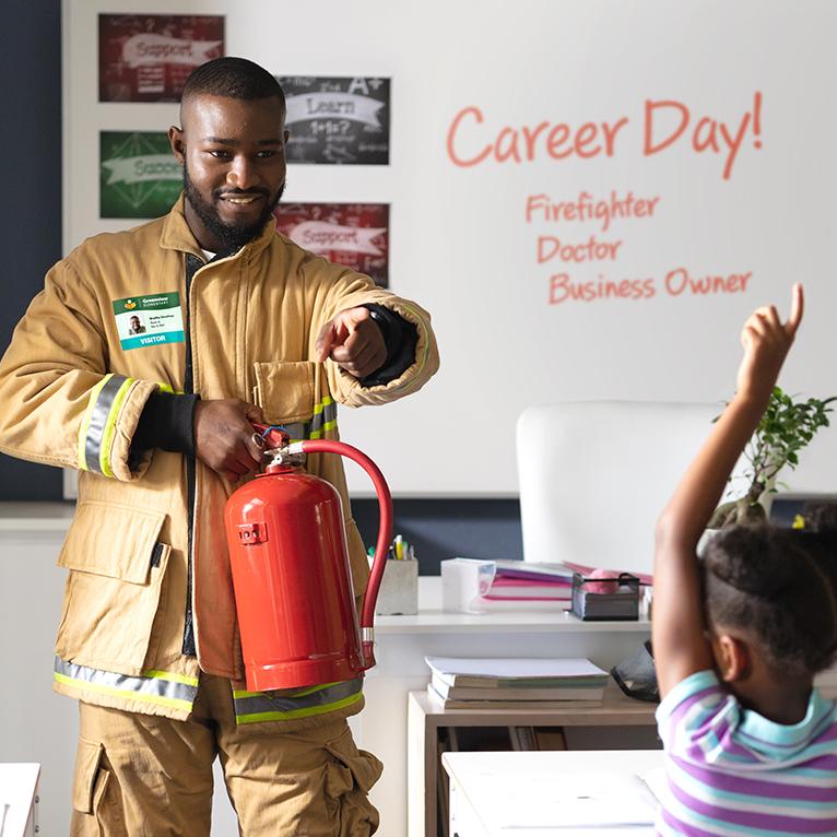 An elementary school visitor with a colorful ID badge giving a class presentation.