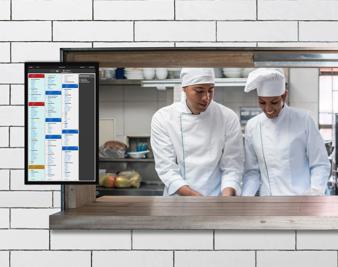 Chefs in a kitchen next to a monitor showing KDS software