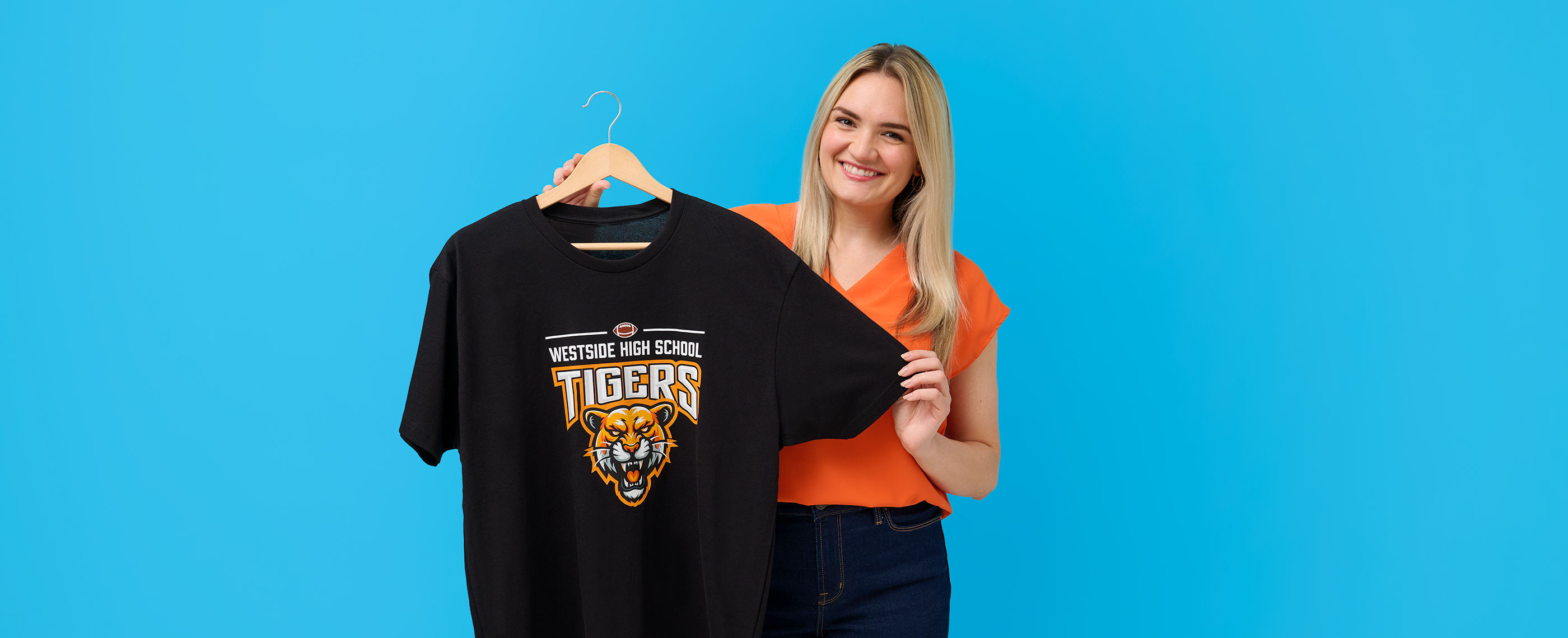 Smiling woman holding t-shirt printed with high school football tiger mascot design.