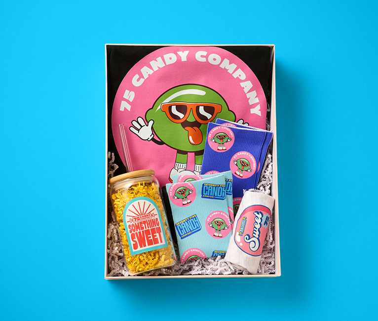 A gift box containing socks, t-shirts, glass tumbler and baby onesie printed with candy designs.